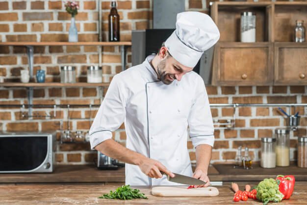 happy-young-male-chef-cutting-red-chili-with-knife-kitchen-counter_23-2147863496